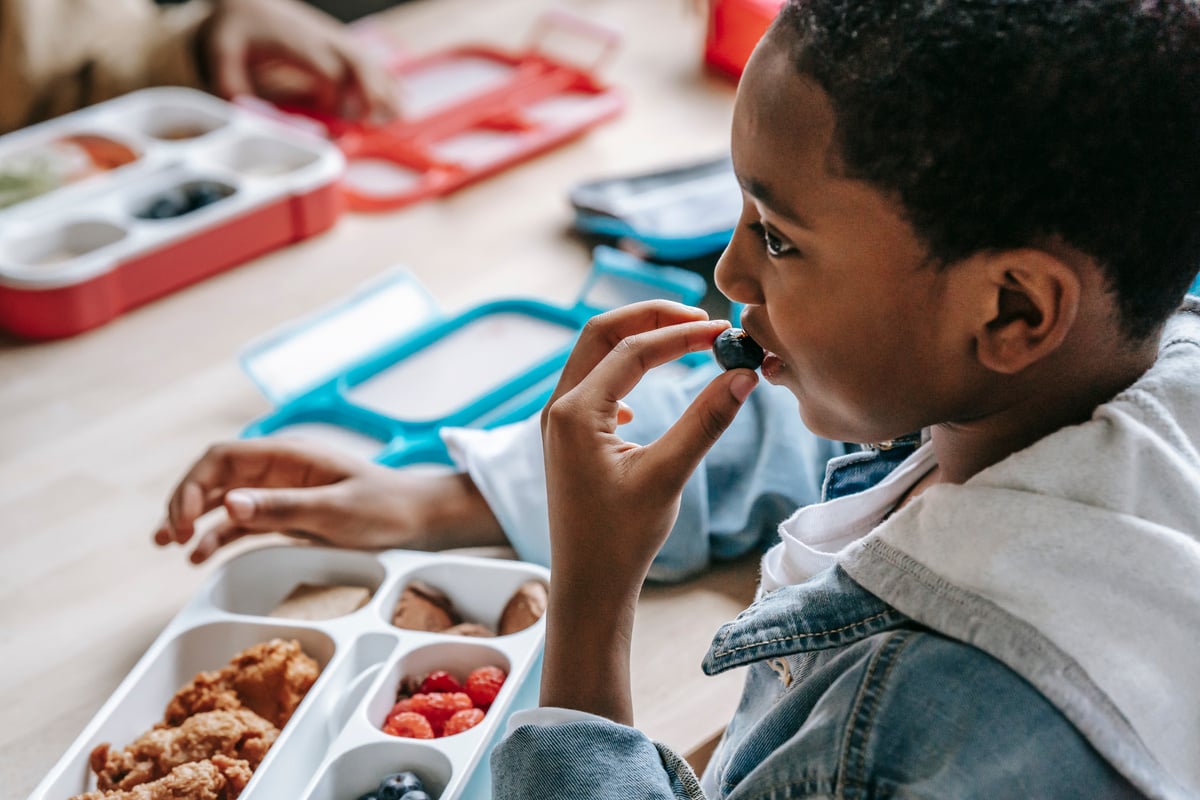 Crop black boy eating blueberries in school